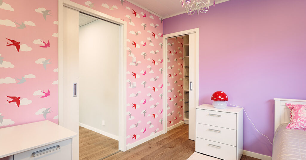 Porta a scomparsa con finiture esterne di colore bianco e carta da parati rosa, nuovole e uccellini rossi.